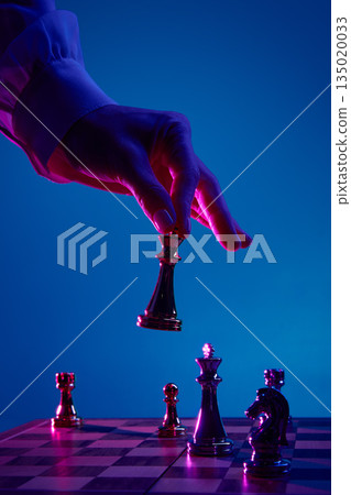 Female fingers holding metallic chess queen mid move. 135020033