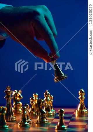 Hand lifting chess piece above board mid move. Hand lifting chess piece above board mid move. 135020039