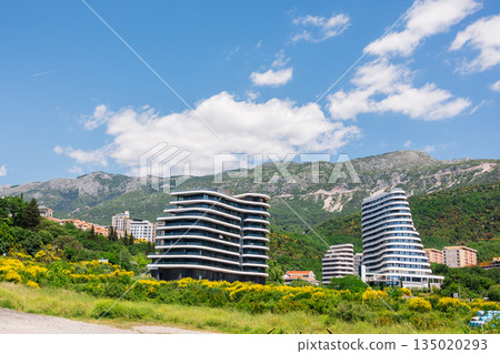 Modern residential buildings in Montenegro surrounded by green hills and mountains. Urban growth, property development, and contemporary lifestyle shaped by nature and architectural planning. 135020293