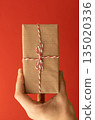 hand holding craft wrapped gift over red background 135020336