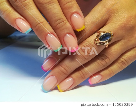 Colorful French Tips Manicure. Hands showcasing natural nails with colorful French tips in pink, yellow, blue and green shades topped with glossy finish. Colorful French Tips Manicure. Hands showcasing natural nails with colorful French tips in pink, yellow, blue and green shades topped with glossy finish. 135020399