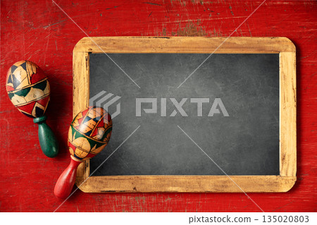 Cinco de Mayo-inspired flat lay featuring maracas and chalk board on a vintage red background 135020803