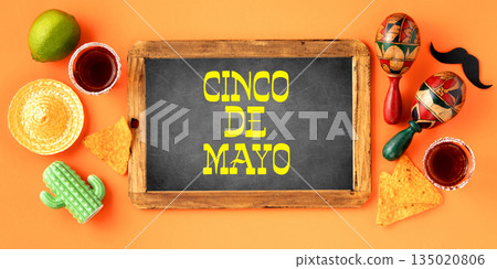 A vibrant Cinco de Mayo-inspired flat lay featuring vintage chalk board, maracas, tequila shots, lime, nacho chips on a bright orange backdrop A vibrant Cinco de Mayo-inspired flat lay featuring vintage chalk board, maracas, tequila shots, lime, nacho chips on a bright orange backdrop 135020806