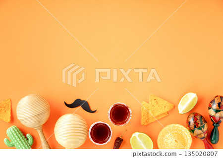 A vibrant Cinco de Mayo-inspired flat lay featuring a sombrero, maracas, tequila shots, lime, chili peppers, nacho chips on a bright orange backdrop banner A vibrant Cinco de Mayo-inspired flat lay featuring a sombrero, maracas, tequila shots, lime, chili peppers, nacho chips on a bright orange backdrop banner 135020807