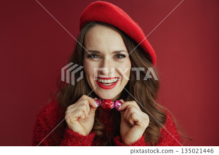 smiling stylish woman in red sweater and beret with candy 135021446