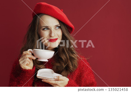 pensive modern female in red sweater and beret with tea cup 135021458