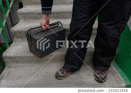 worker puts a heavy iron toolbox on a concrete staircase 135021856