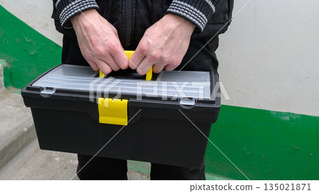 male hands close up holding a black toolbox by the yellow handle male hands close up holding a black toolbox by the yellow handle 135021871