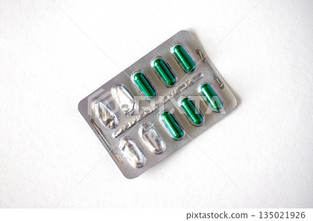 Semi-empty metal blister pack with green capsules isolated on white background. Metal blister for capsules 135021926