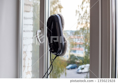 Cleaning robot cleans the inside of apartment windows. Modern household cleaning products. Modern device for removing dirt from glass. Cleaning robot cleans the inside of apartment windows. Modern household cleaning products. Modern device for removing dirt from glass. 135021928