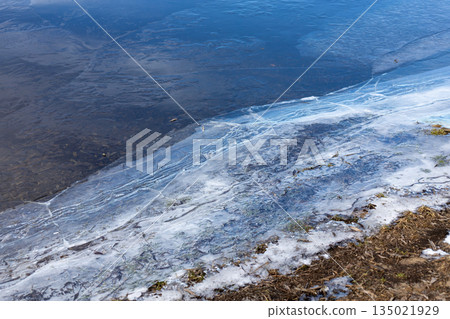 Cracked ice on the river bank. The beginning of spring ice drift. Melting ice and snow. Thin layer of cracked ice on the grass on the river bank Cracked ice on the river bank. The beginning of spring ice drift. Melting ice and snow. Thin layer of cracked ice on the grass on the river bank 135021929