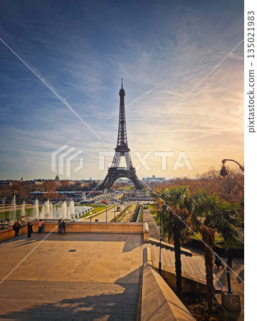 Stunning silhouette of the Eiffel Tower in Paris against a hazy sunset sky, with a look down over the Jardins du Trocadero fountains and toward Champ de Mars Stunning silhouette of the Eiffel Tower in Paris against a hazy sunset sky, with a look down over the Jardins du Trocadero fountains and toward Champ de Mars 135021983