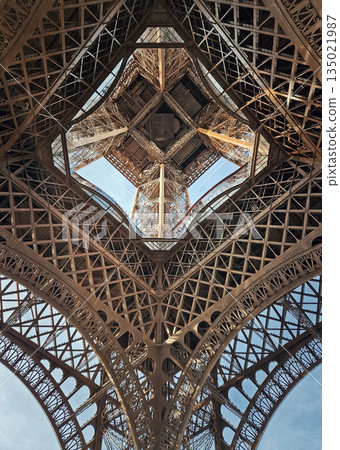 A mesmerizing look up into the intricate iron heart of the Eiffel Tower, through massive lattice arches, revealing the complex geometric engineering and the internal elevators ascending toward the sky A mesmerizing look up into the intricate iron heart of the Eiffel Tower, through massive lattice arches, revealing the complex geometric engineering and the internal elevators ascending toward the sky 135021987