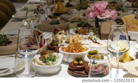 Luxury banquet table with Mediterranean mezze appetizers, pink rose centerpieces and wine creating elegant dining event atmosphere 135022011