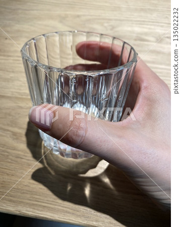 Hand holding empty glass with sunlight creating shadows on wooden table background 135022232