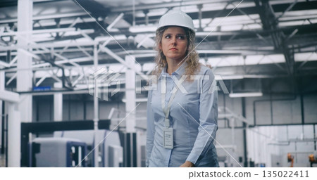 Curly Haired Woman Wearing Protective Helmet Moves Calmly Across High Tech Factory Floor 135022411
