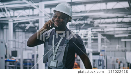 Industrial Engineer Walks Through High Tech Factory Floor While Talking on Smartphone and Smiling 135022418