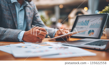 Business professional analyzing financial data on tablet and laptop 135022558