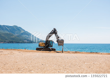 Excavator working on a coastal area near the sea. Infrastructure preparation, human intervention, and landscape transformation within seaside development. Excavator working on a coastal area near the sea. Infrastructure preparation, human intervention, and landscape transformation within seaside development. 135022721