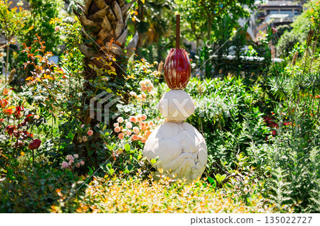 Decorative garden sculpture surrounded by lush greenery and flowering plants. Artistic landscape design, outdoor aesthetics, creative expression and serene residential garden atmosphere 135022727
