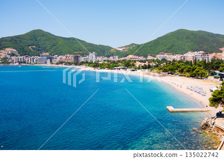 Panoramic view of Budva bay with city beach and mountains. Coastal urban harmony, summer tourism appeal, Mediterranean scenery, and relaxed seaside atmosphere in Montenegro Panoramic view of Budva bay with city beach and mountains. Coastal urban harmony, summer tourism appeal, Mediterranean scenery, and relaxed seaside atmosphere in Montenegro 135022742