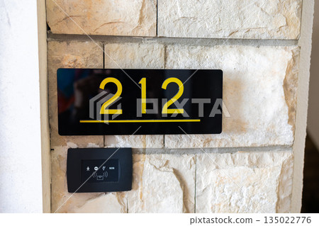 Apartment door 212 number sign mounted on stone interior wall surface. Residential navigation, building identification system, interior architecture detail and organized accommodation environment Apartment door 212 number sign mounted on stone interior wall surface. Residential navigation, building identification system, interior architecture detail and organized accommodation environment 135022776