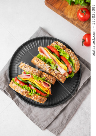 Two sandwiches with ham, cheese, lettuce and vegetable on a black plate on a concrete background 135023093