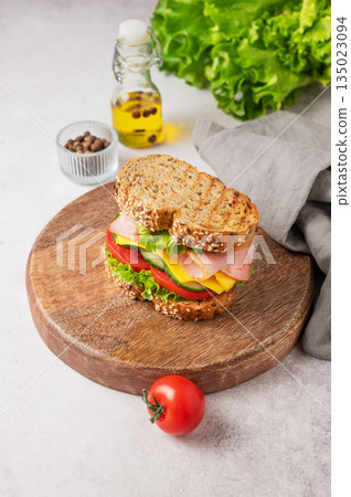 Sandwich with ham, cheese, lettuce and vegetable on a wooden board on a concrete background 135023094