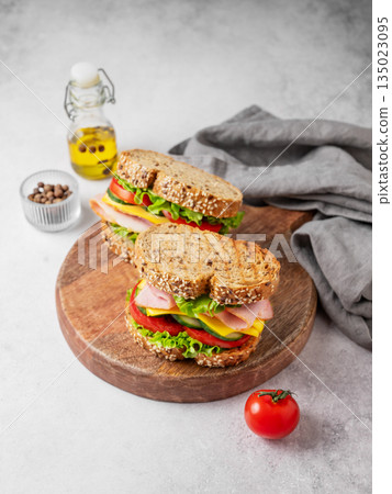 Two sandwiches with ham, cheese, lettuce and vegetable on a wooden board on a concrete background 135023095