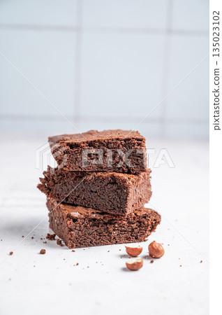 Pieces of chocolate brownie on a light background with nuts close up. 135023102