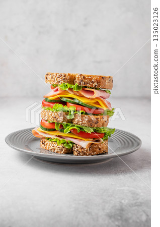 A triple sandwich with ham, cheese, lettuce, and vegetables on whole grain bread on a plate A triple sandwich with ham, cheese, lettuce, and vegetables on whole grain bread on a plate 135023126
