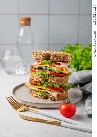 A triple sandwich with ham, cheese, lettuce, and vegetables on whole grain bread on a plate 135023127