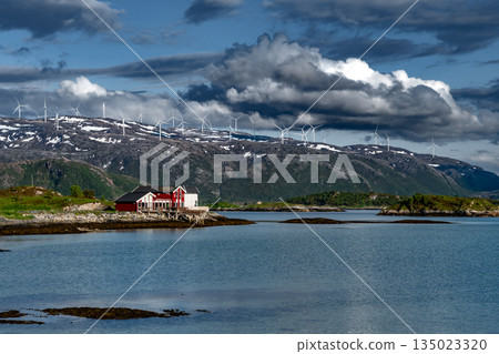 Coastal Landscape With Calm Fjord, Snowy Mountains With Wind Turbines And Cottages On Sommaroy Island In Norway Coastal Landscape With Calm Fjord, Snowy Mountains With Wind Turbines And Cottages On Sommaroy Island In Norway 135023320