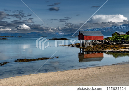 Sandy Beach And Red Hut Cottage In Front Of Mountains On Sommaroy Island At Calm Fjord In Norway Sandy Beach And Red Hut Cottage In Front Of Mountains On Sommaroy Island At Calm Fjord In Norway 135023324