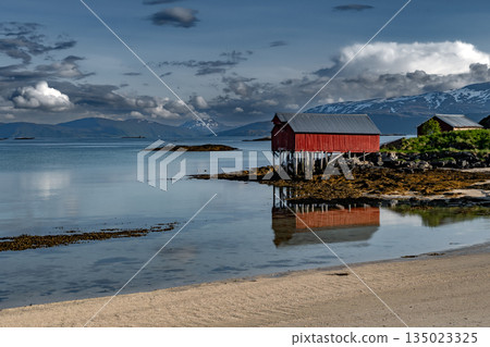 Sandy Beach And Red Hut Cottage In Front Of Mountains On Sommaroy Island At Calm Fjord In Norway Sandy Beach And Red Hut Cottage In Front Of Mountains On Sommaroy Island At Calm Fjord In Norway 135023325