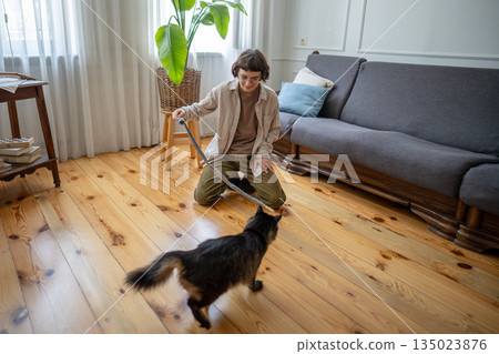 Woman engaging domestic cat in active play, trigger hunting behavior, feline leaping and chasing toy Woman engaging domestic cat in active play, trigger hunting behavior, feline leaping and chasing toy 135023876