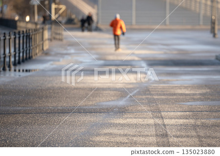 People walking on asphalt sidewalk road covered with technical salt on sunny frosty winter day. People walking on asphalt sidewalk road covered with technical salt on sunny frosty winter day. 135023880