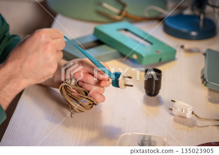 Craftsman carefully removes blue electrical tape wrapped around old plug, upcycling hobby and repair 135023905
