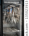 Dried salted fish snacks selling in local fishmonger, stored in big refrigerator with price tags. 135023913