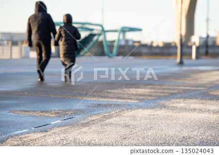 Couple walking on asphalt sidewalk road coated with special chemicals and technical salt in winter. Couple walking on asphalt sidewalk road coated with special chemicals and technical salt in winter. 135024043