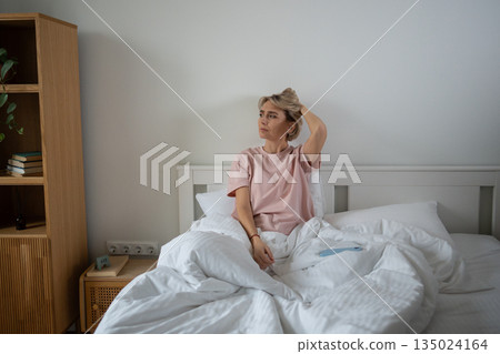 Unmotivated restless middle aged woman procrastinating in bed after waking up, exhausted expression. 135024164