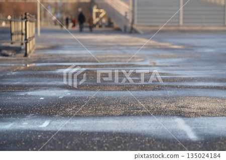 Deicing chemicals on asphalt in winter. Salt grains on icy sidewalk paving slab with technical salt 135024184