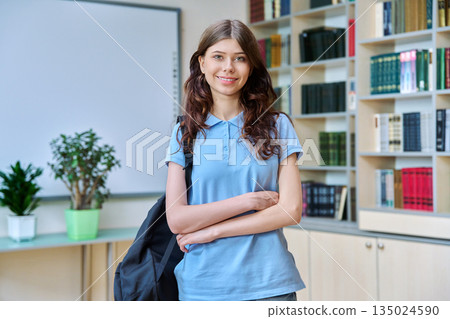 Portrait of teenage smiling girl high school student posing in library classroom Portrait of teenage smiling girl high school student posing in library classroom 135024590