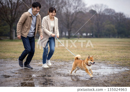 一對夫婦和一隻小柴犬在冬天的泥地奔跑玩耍 一對夫婦和一隻小柴犬在冬天的泥地奔跑玩耍 135024963