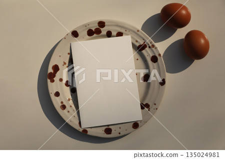 Minimal Food Concept Still Life with Blank greeting Card on Ceramic Plate with Brown splashes, Eggs. Creative Cooking Background, Recipe Mockup, Modern Editorial Easter Flat Lay, Top View. 135024981