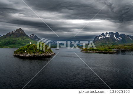 Coastal Landscape With Lighthouse And Snowy Mountains Near Stokmarknes At The Lofoten In Norway Coastal Landscape With Lighthouse And Snowy Mountains Near Stokmarknes At The Lofoten In Norway 135025103