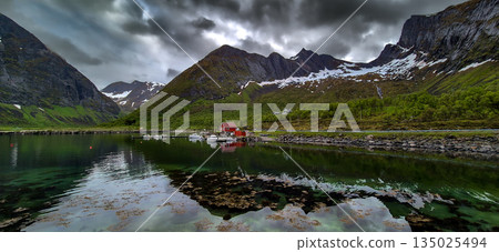 Calm Fjord With Boats And Red Huts In Front Of Snowy Mountains On Senja Island In Norway Calm Fjord With Boats And Red Huts In Front Of Snowy Mountains On Senja Island In Norway 135025494