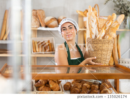 Young saleswoman displays baguettes in wicker basket 135026174