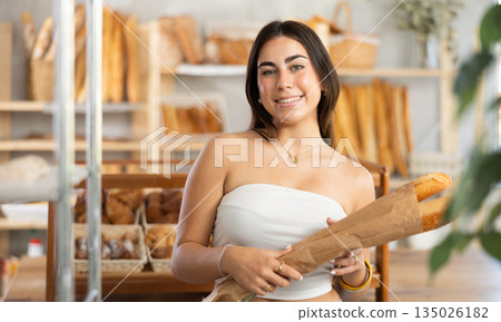 Positive young girl holding baguettes in paper bag Positive young girl holding baguettes in paper bag 135026182