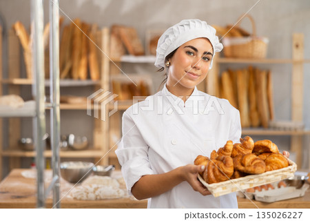Young saleswoman displays croissants in square wicker basket 135026227